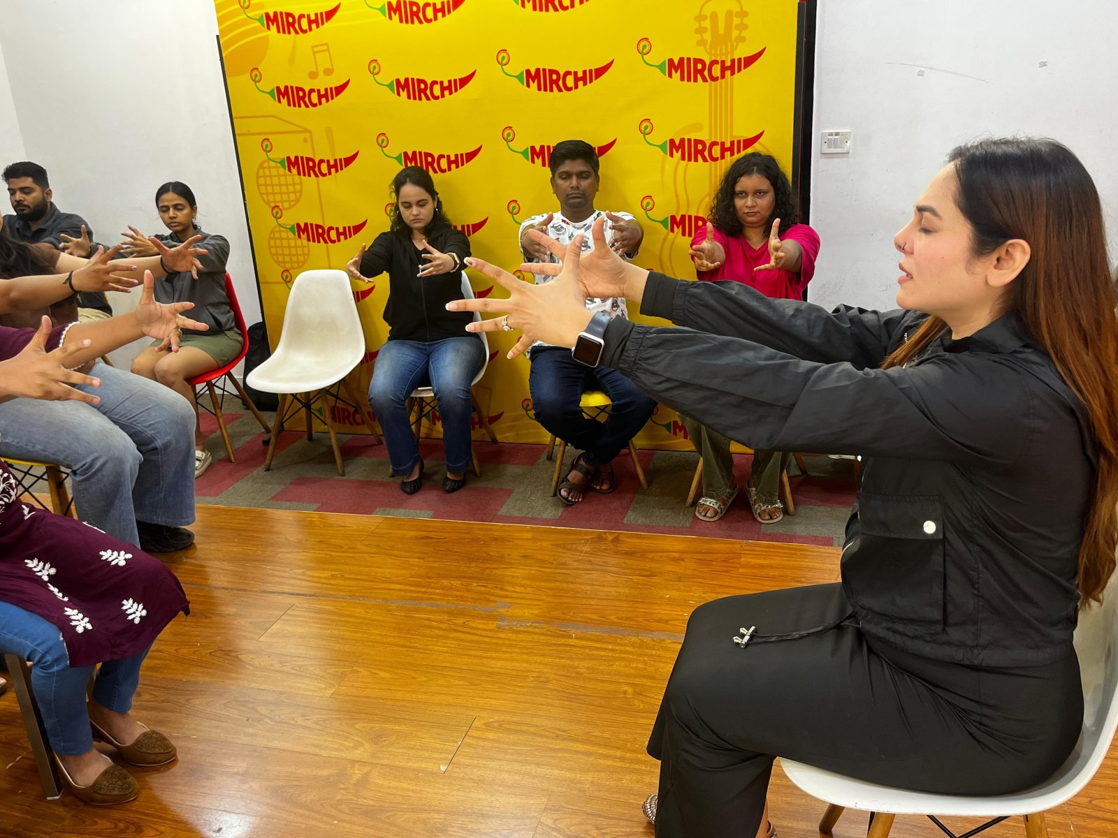 Vibha Jain seated facing a semicircle of participants, guiding them through a hands-extended relaxation exercise during a group workshop.