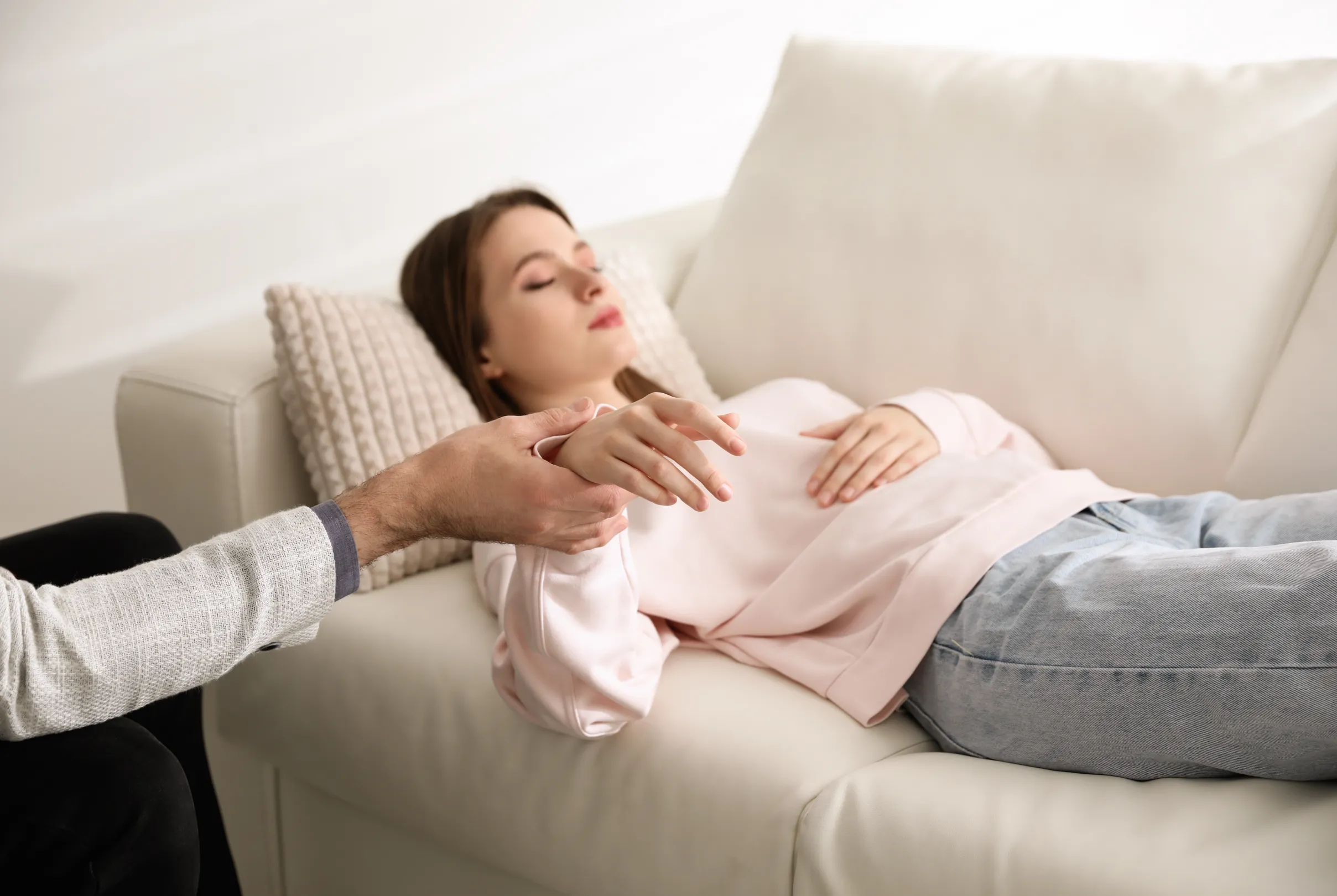 A person reclining calmly on a sofa with eyes closed during a guided relaxation session with a practitioner.