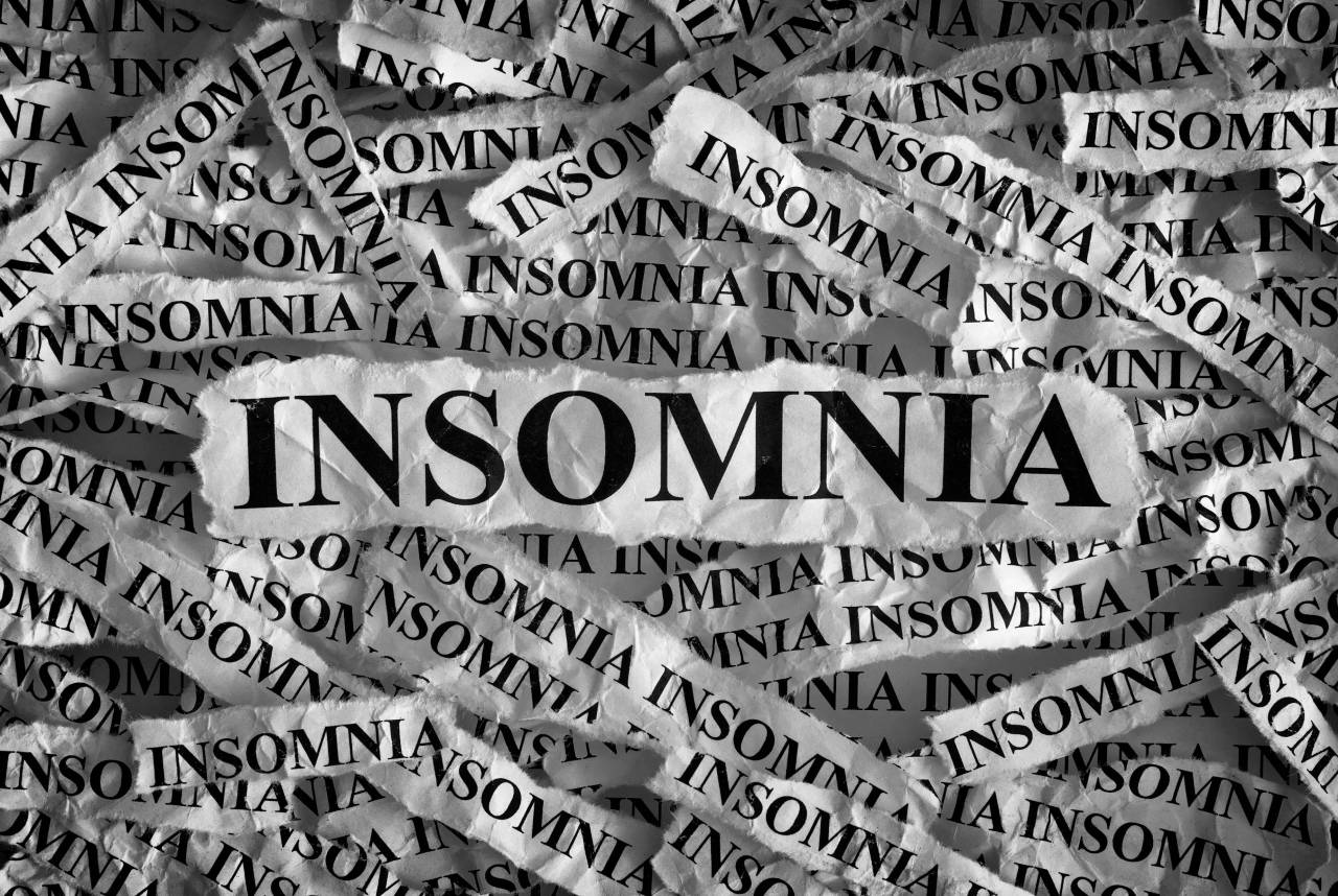 Torn strips of newspaper, each printed with the word insomnia, layered on top of one another.