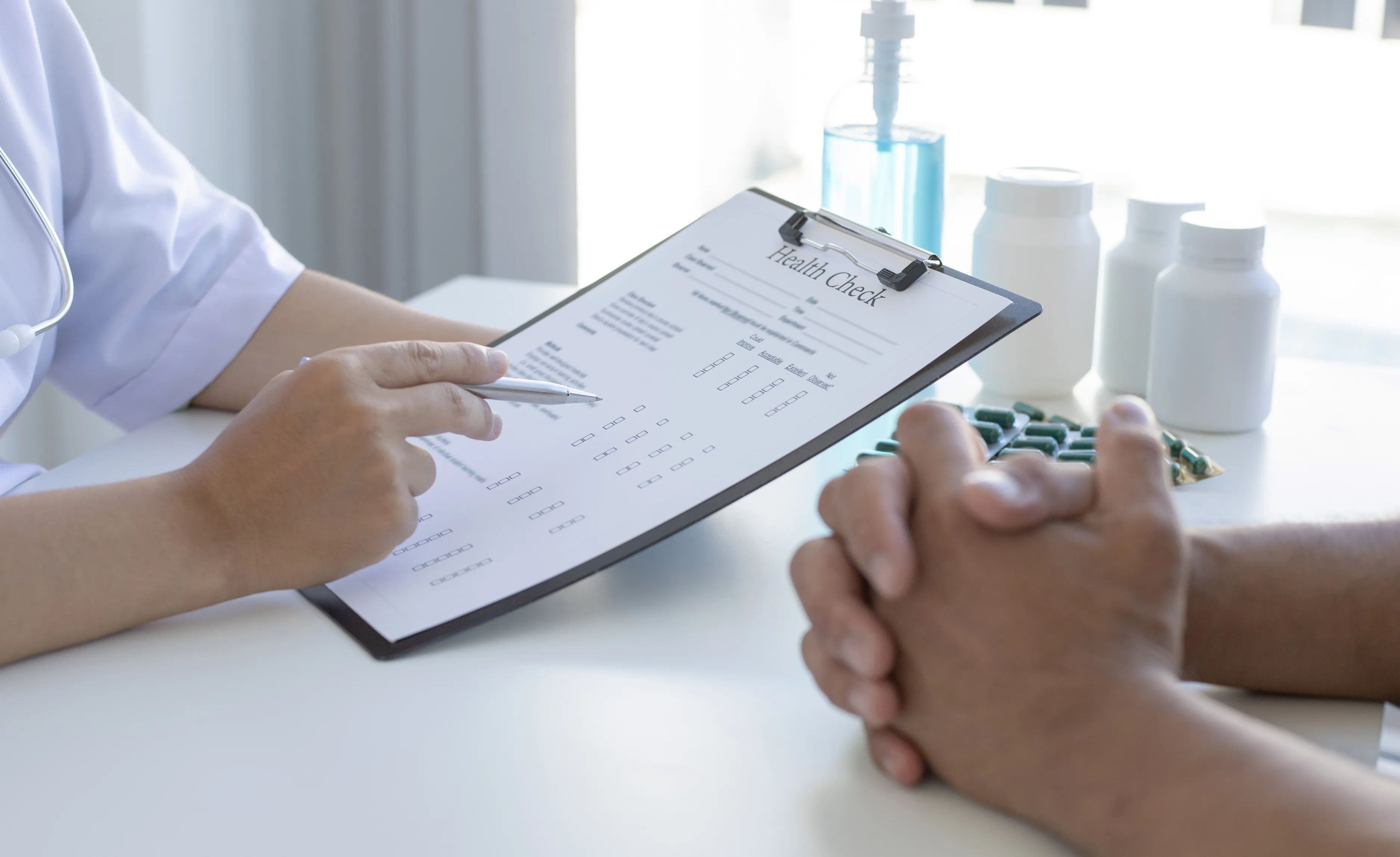 A healthcare professional discussing a health check form with a patient across a desk.