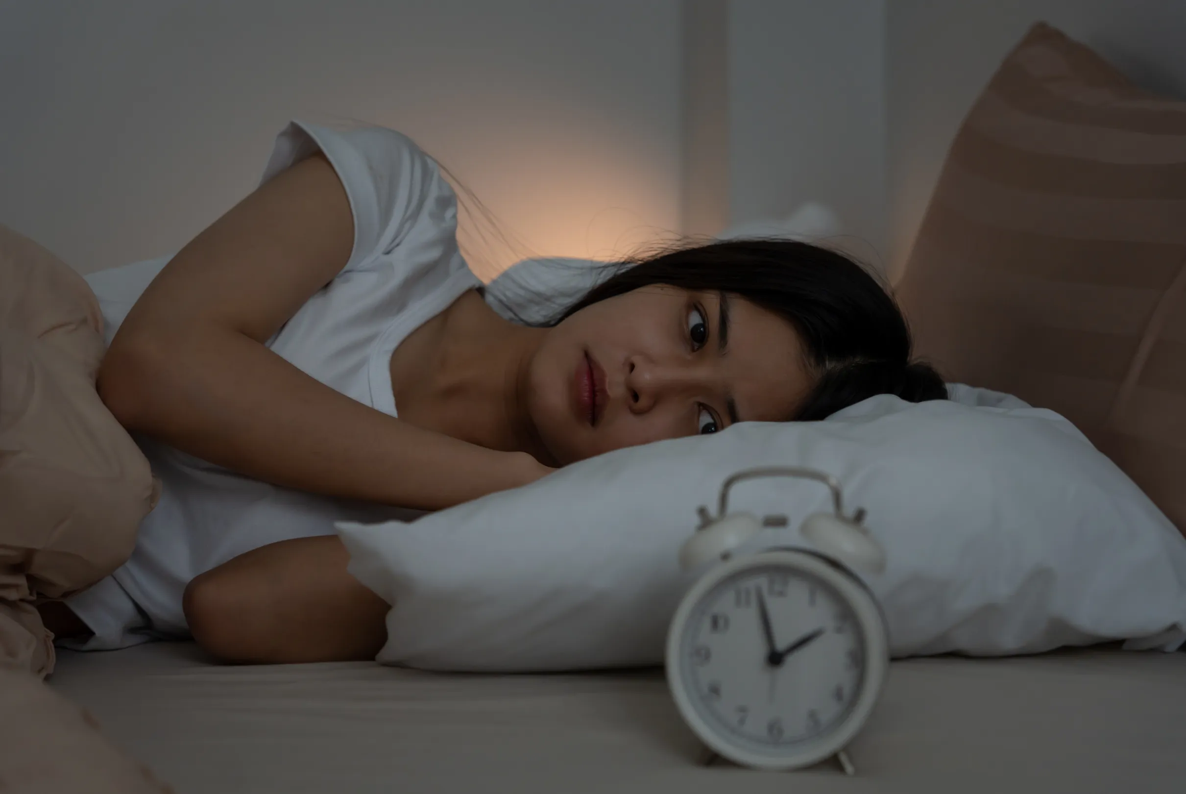 A dimly lit bedroom at night with a person resting and a small alarm clock nearby.