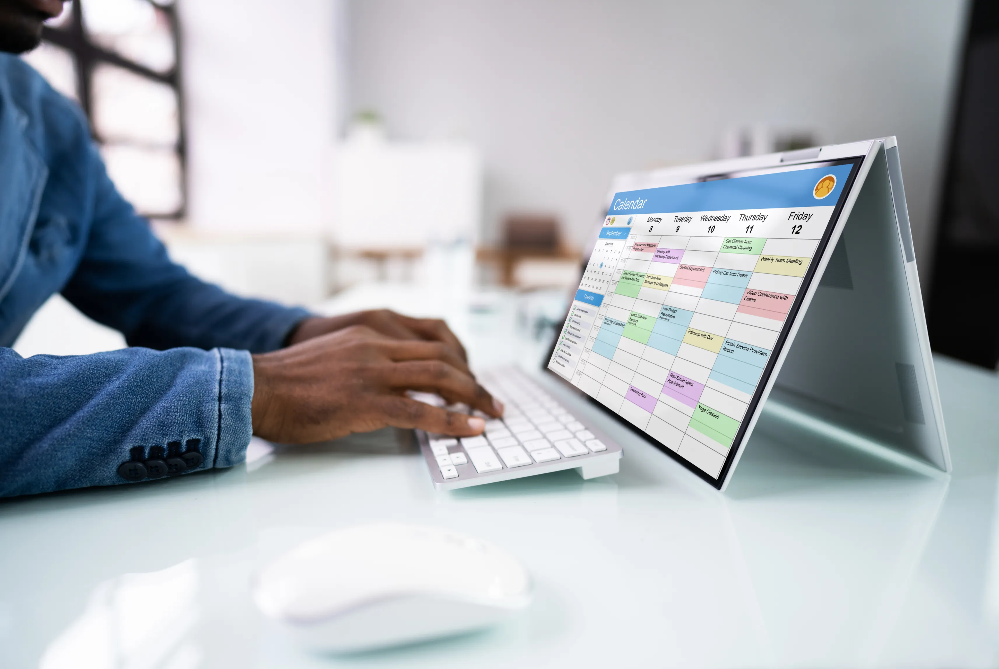 A person working at a laptop showing a densely filled weekly calendar.
